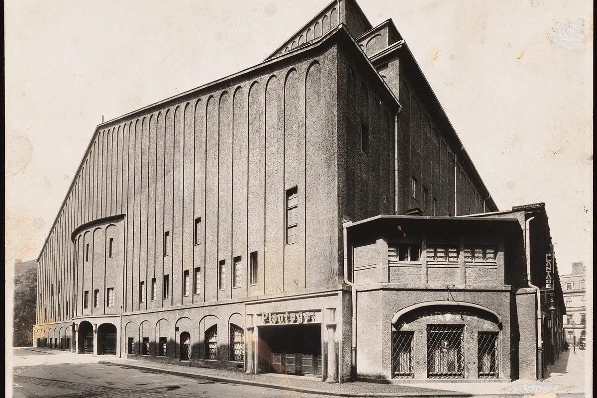 A large brick theatre building with tall arched openings and a stepped roof, photographed from the street in black and white